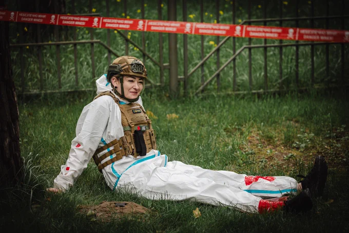 A woman in protective equipment takes part in a simulated emergency scenario inside a marked hazardous area during tactical medical training