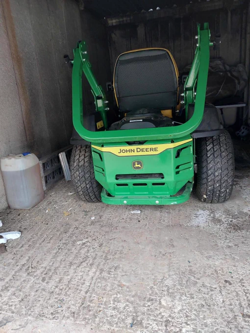 A green JOHN DEERE ride-on mower located inside garage.