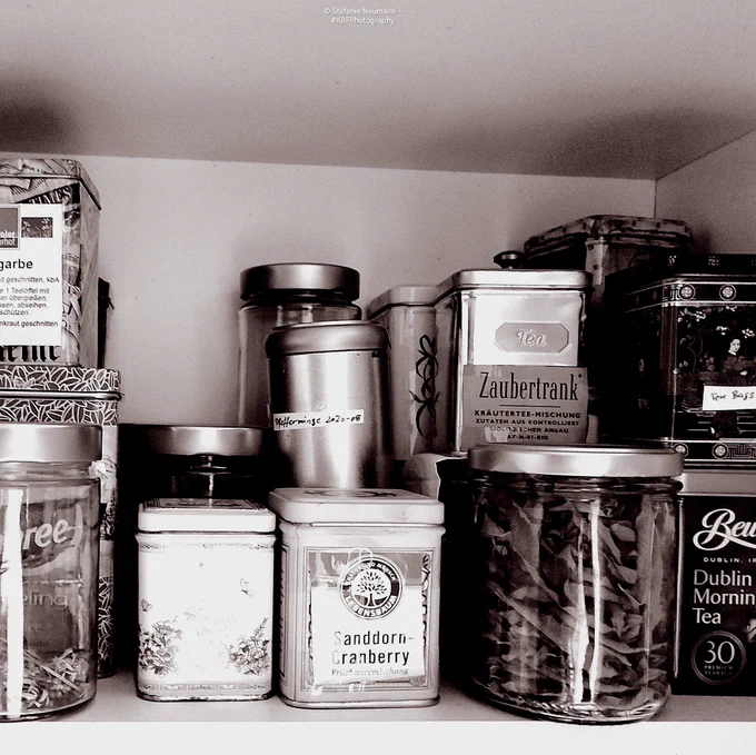 View into a cupboard with a selection of teas and herbs on a shelf. Black-and-white picture with a pink filter.

© Stefanie Neumann - #KBFPhotography 
