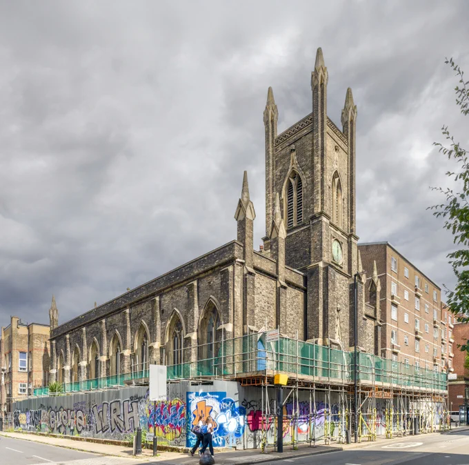 A Gothic Revival style church under renovation, surrounded by scaffolding and bright graffiti-covered hoardings. 