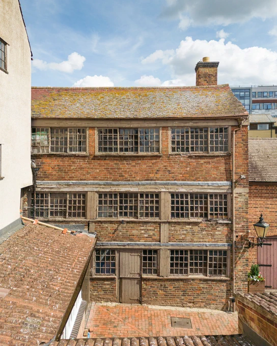 A historic brick building with three floors of large, grid-patterned windows and wooden beams.
