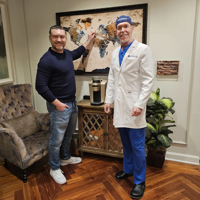 Dr. Ken Anderson with a patient from London in the lobby at Anderson Center for Hair in Alpharetta adding a pin to the map that shows the location of all the patients at the practice.