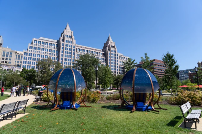 Franklin Park in Washington, DC with an art installation, bright green grass, benches, and buildings in the background.