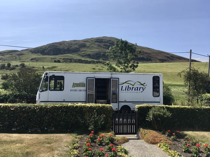 An image of a mobile library van parked outside on a street on a sunny day. 