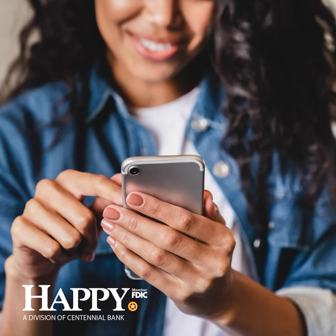 Smiling woman in a denim jacket using a smartphone, focusing on her hands and device interaction.