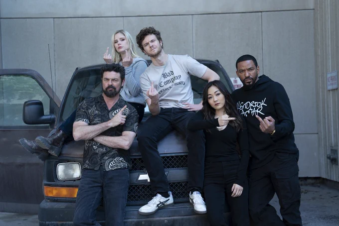 Karl Urban, Erin Moriarty, Jack Quaid, Karen Fukuhara, and Laz Alonso on the set of The Boys. They’re giving the middle finger to the camera as they sit on top of aand beside a van.