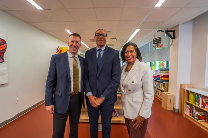 Mayor Bowser, Chancellor Ferebee, and Principal Brigham Kiplinger stand smiling a posed photo in the library of Garrison Elementary School.