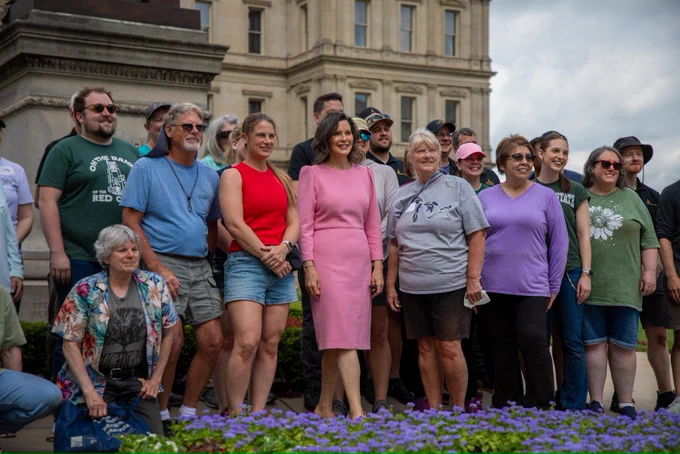 Gov. Whitmer takes a photo in front of Michigan Capitol flowers alongside volunteers.