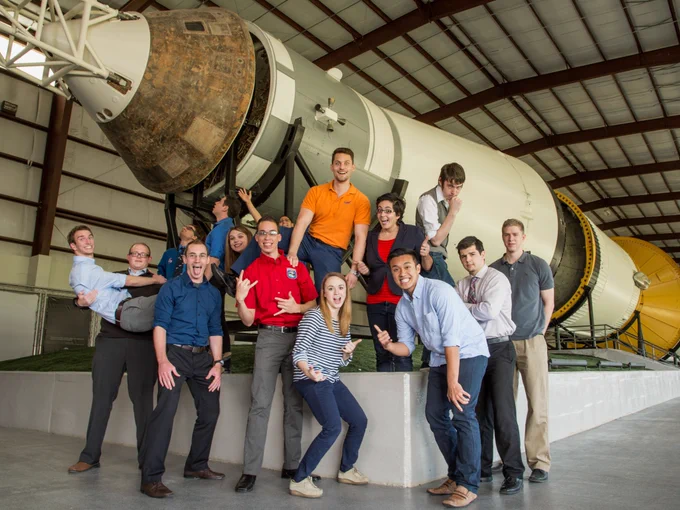 A group of NASA's Johnson Space Center interns pose for a lighthearted photo in the Saturn V facility. They make silly faces and gestures while standing in front of the Saturn V rocket. Credit: NASA