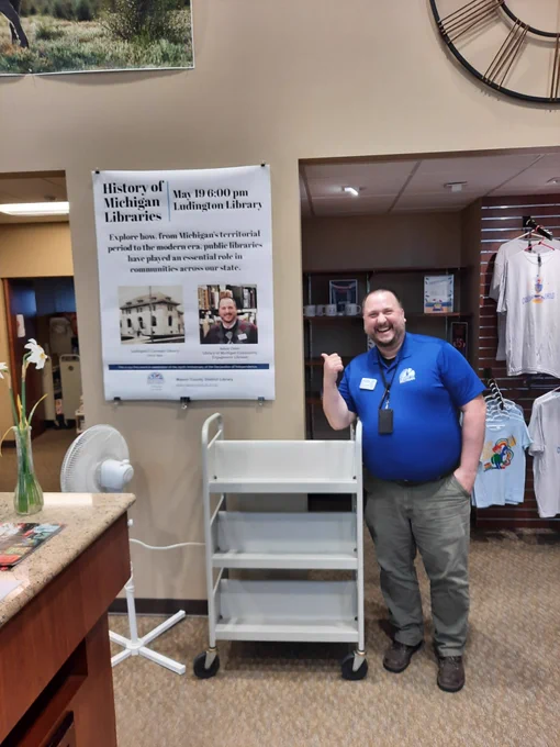 Community Engagement Librarian Adam Oster pointing at a sign of his program while inside the Ludington Library.