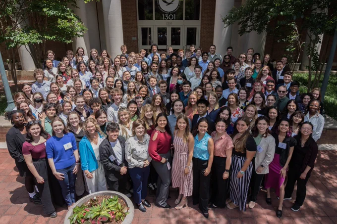 A group photo of approximately 150 people young adults in business casual clothing. The group is posing outside in front a building with a NOAA logo on the door.