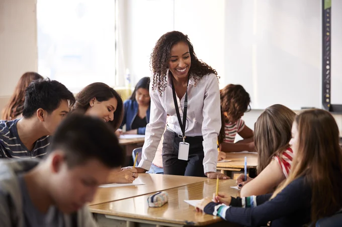 A teacher speaks with high school students working at their desks. 
