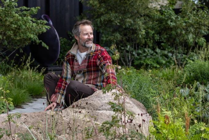 Garden designer Angus Thompson is sitting in the Asthma and Lung UK Breathing Space garden at Chelsea Flower Show.