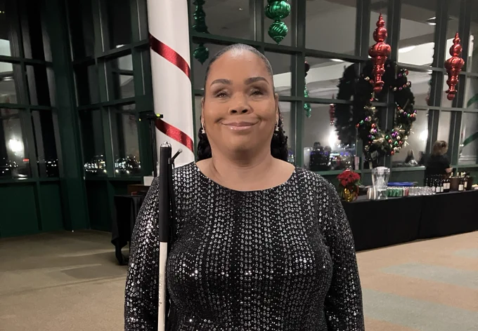 Latonya smiles, wearing a black long-sleeve sequin dress, with her white cane beside her. 