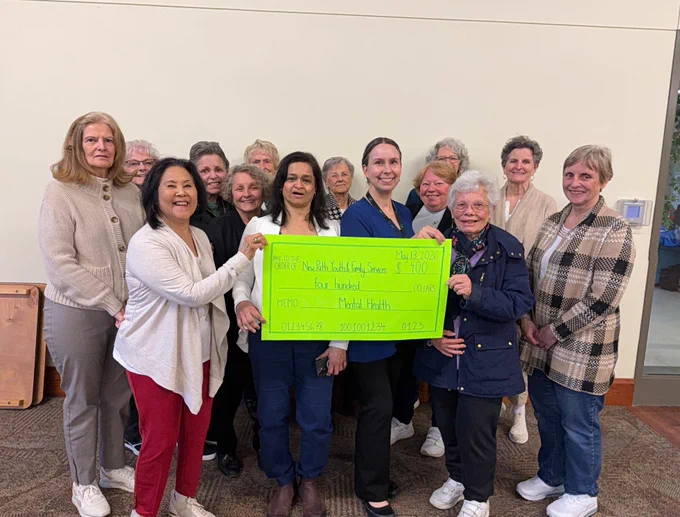 Group of people standing indoors holding a large green check for a charitable donation.