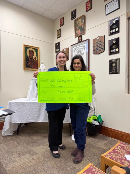 Two women holding a large bright green check for $400 in an office decorated with plaques and religious artwork.