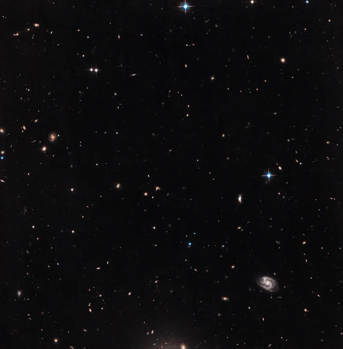 Background galaxies and stars are sprinkled across a black background. Some of the distant galaxies are spirals.