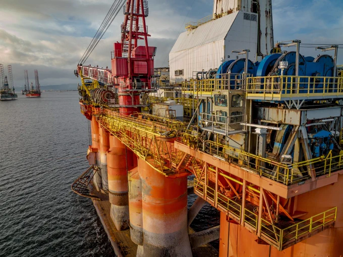 A multicolored offshore oil rig, painted in orange, red, yellow, and blue, sits in the ocean with a partly cloudy sky above.  