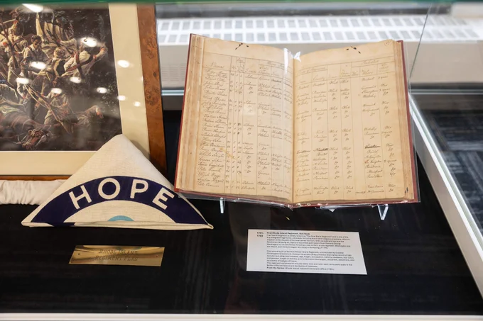 close up in display case of flag folded into triangle with text hope visible and old log book with names and other info
