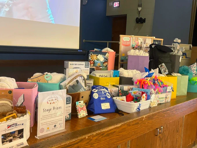 A variety of gift baskets and boxes are arranged on a stage, containing items like stuffed animals, bath products, and colorful toys.