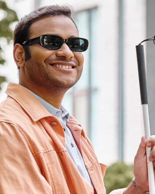  A man wearing sunglasses holding a white cane. 