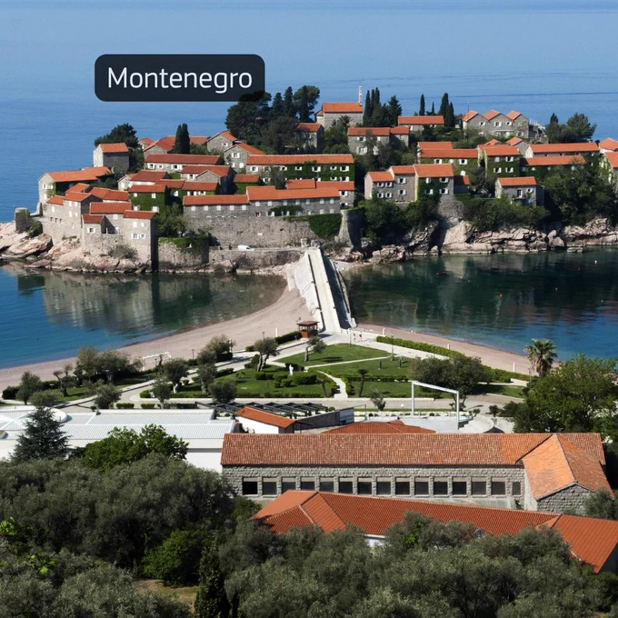 Image of a coastal area in Montenegro with stone buildings, red rooftops, and a narrow road leading across the water.