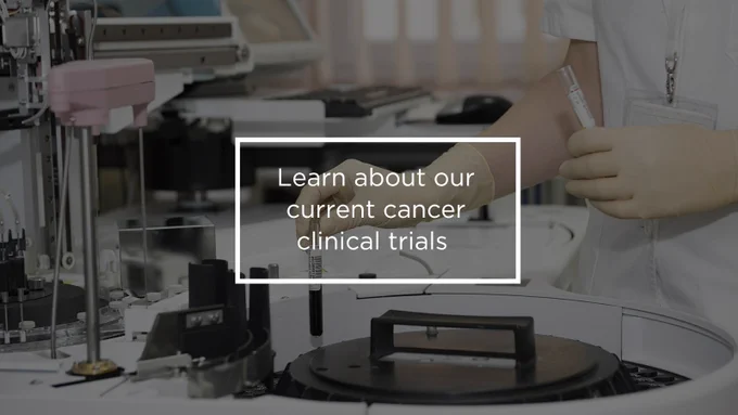 A person is working in a laboratory near scientific equipment. A transparent box in the image contains the text: "Learn about our current cancer clinical trials."