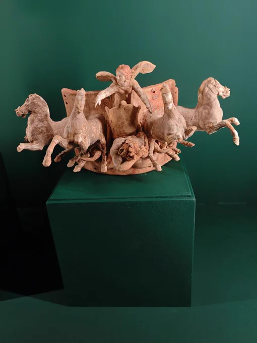TERRACOTTA APPLIQUE WITH NIKE AND QUADRIGA, C. 240 BCE. MUSEO NAZIONALE ROMANO

This applique was found in a dig on the Cælian hill under via S. Stefano Rotondo, in a tomb. Here we see a curved plaque with holes at the back, to attach it to the neck of a giant urn. Bursting out from it in high relief is a quadriga pulled by four galloping horses, all with traces of paint. In the chariot, leaning forward as she is pulled by the impatient horses' invisible reins, is Nike or Victory, and under her chariot is a Giant, turning his head to the left as he dies under her wheels. This pathos came with the conquest of Magna Græcia, and the arrival in Rome of coroplasts, clay-workers, from Apulia and Sicily, c. 250 BCE. In that moment, Rome was no longer just a regional Latin power, but had not yet become the massive, cynical, marble-clad empire of the late Republic. It represented a brief, brilliant window of artistic synthesis: southern Greek energy bursting out of a Republican Roman tomb.