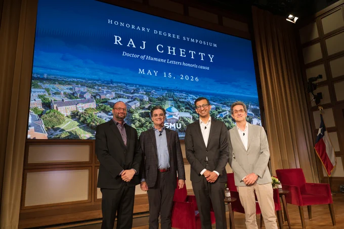 Four individuals stand on a stage in front of a large screen that reads "Honorary Degree Symposium, Raj Chetty, Doctor of Humane Letters honoris causa, May 15, 2026, SMU." The background displays an aerial view of a campus. Chairs and a flag are visible on the right side of the stage.
