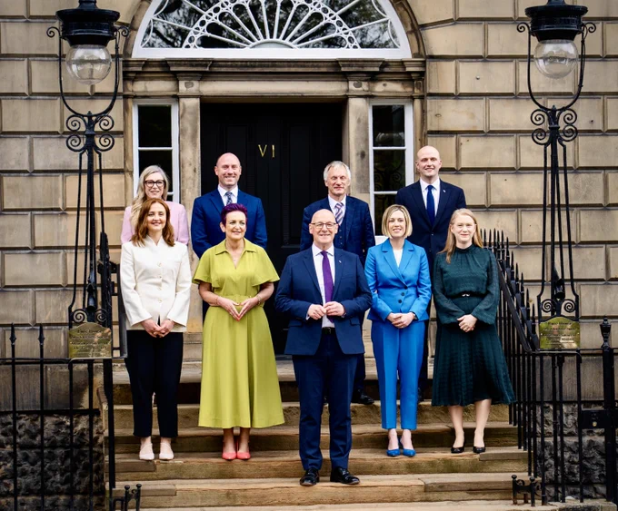 Group photo of the Scottish Cabinet on the steps of Bute House, in front of the black door - from left to right: Mairi McAllan, Gillian Martin, Neil Gray, Angela Constance, John Swinney, Ivan McKee, Jenny Gilruth, Stephen Flynn, Shirley-Anne Somerville.