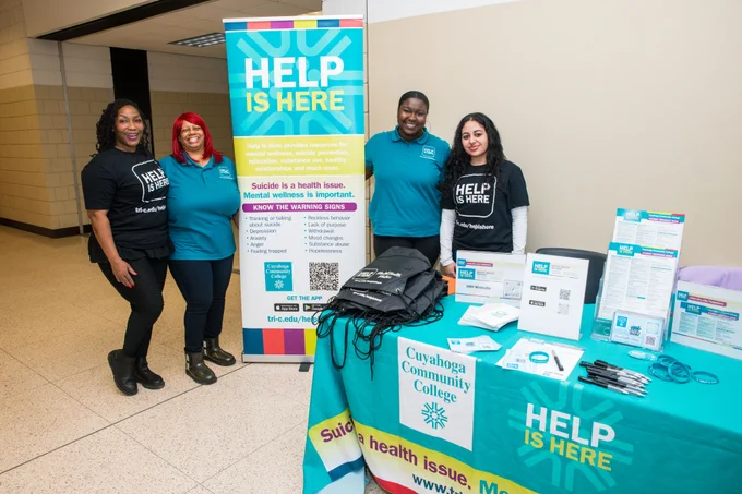 Four people standing next to a sign and table that say "Help is Here"