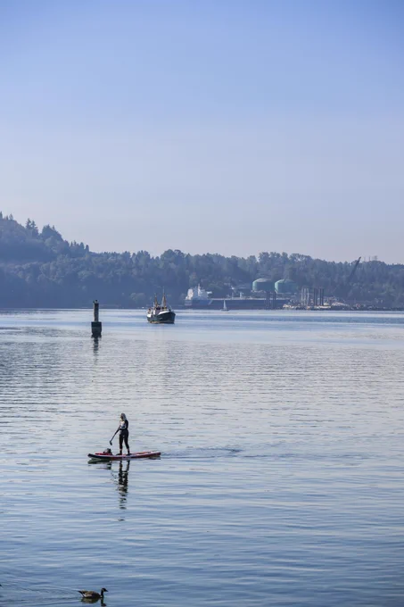 Scenic view of peaceful water with a person on a paddle board, a large vessel and mountains in the distance. 
