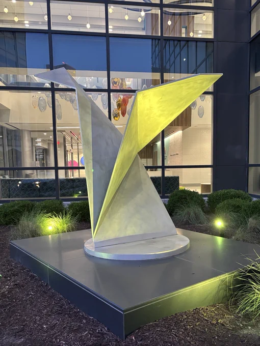 An origami statue in front of a hospital, illuminated in green.