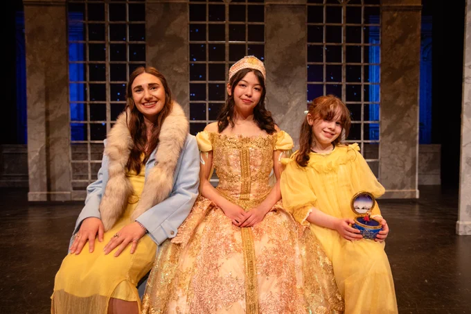 Three actresses of different ages in yellow gowns sitting on a bench