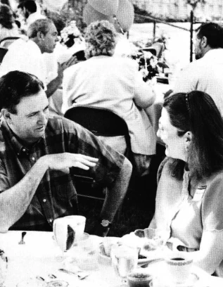 A group of people seated around outdoor tables, engaged in conversation during a social event.