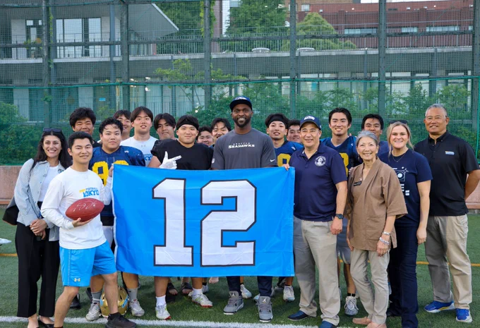 Retired DE Cliff Avril stands with a group of Univ. of Tokyo football players, holding a 12 flag. 
