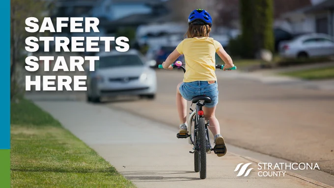 Child wearing a helmet rides a bicycle on a suburban street with the words 'Safer streets start here' over the image