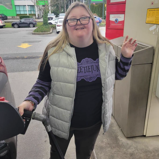 A young woman with diverse abilities smiling while pumping gas, demonstrating the real-world independence skills taught at Pivot Point to help bridge the gap after high school.