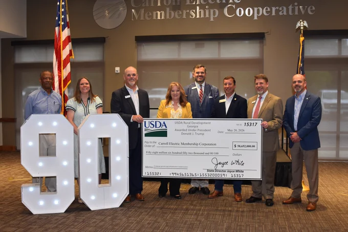State Director Joyce White (wearing yellow suit jacket) is pictured with Georgia EMC and Carroll EMC representatives to present them with a large mock check for $58 million.