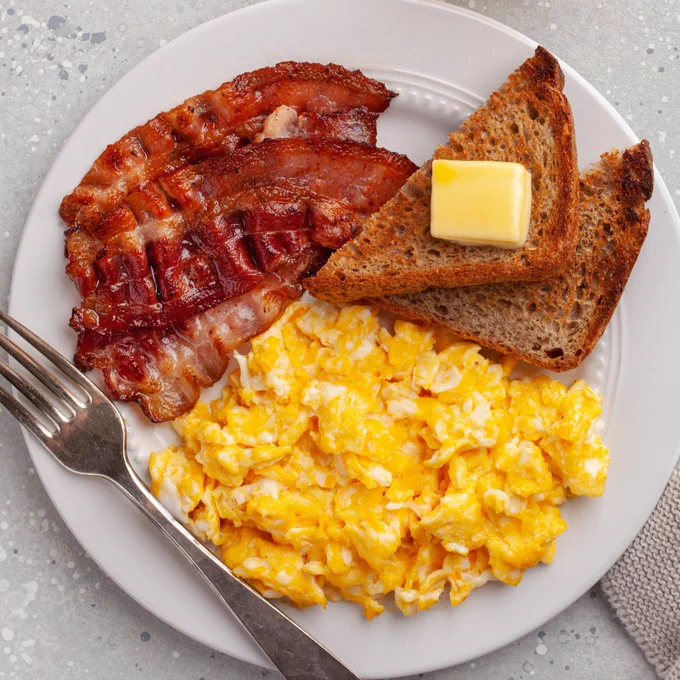 A white plate with scrambled eggs, bacon and toast | Une assiette blanche avec des œufs brouillés, du bacon et des toasts 