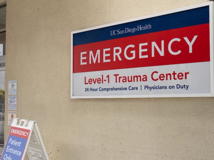 Emergency entrance sign at UC San Diego Health, indicating a Level-1 Trauma Center. The sign mentions 24-hour comprehensive care and physicians on duty. An additional sign directs patients to the entrance.
