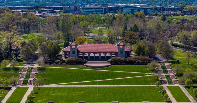 An aerial centers the World's Fair Pavilion as sidewalks zigzag through Government Hill in the foreground while spring trees bud behind the structure. 