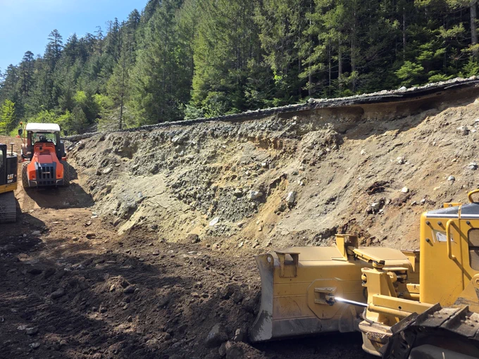 Construction machinery works to rebuild a washed away embankment along a rural section of State Route 20. The damaged highway is seen above.