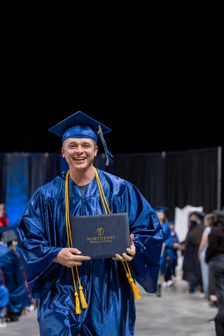An individual wearing a blue graduation cap holds a diploma.
