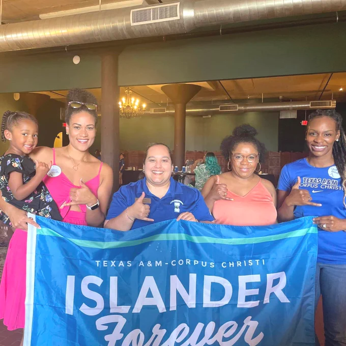 Four TAMU-CC Islander alumni hold a "Texas A&M-Corpus Christi Islander Forever" banner and pose smiling with shakas up hand gestures for a photo.