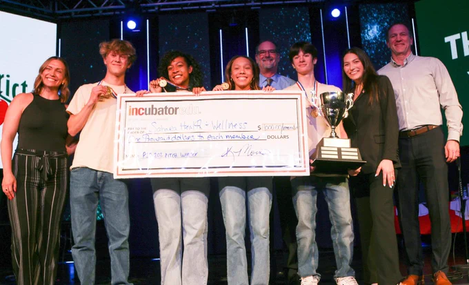 group of students stand on stage with adults holding oversize check