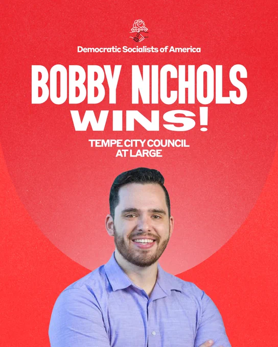 Democratic Socialists of America. Bobby Nichols wins! Tempe City Council at-large. Photo of Bobby, a young man with short dark hair and a beard, looking at the viewer with a warm, can-do smile. His arms are crossed in front of him, and he is wearing a blue button-down shirt.