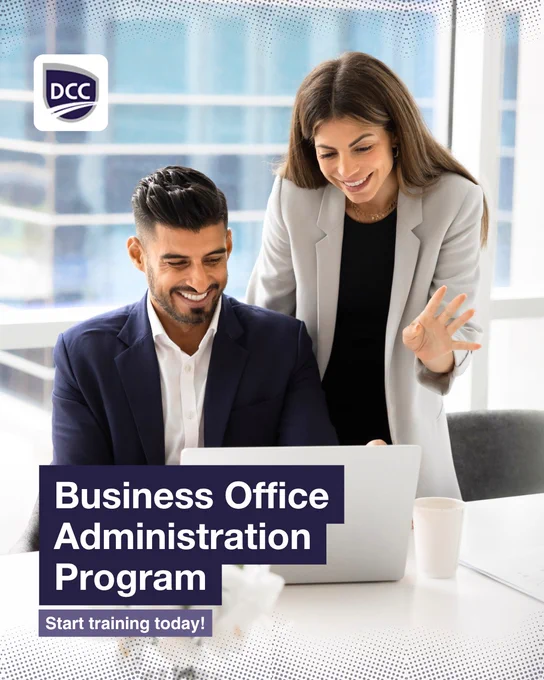 Two office professionals smile while reviewing information on a laptop in a bright workplace setting beside text promoting the Business Office Administration program and training opportunities at Discovery Community College.