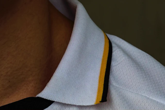 A detailed close-up of a white polo shirt collar with yellow and black stripes. The lighting creates a sharp contrast, adding to the focus on texture.