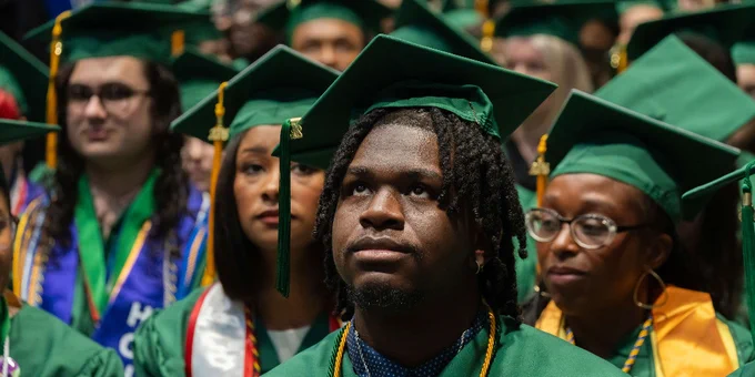 Group of FCC graduates wearing green caps and gowns seated during the Commencement ceremony.